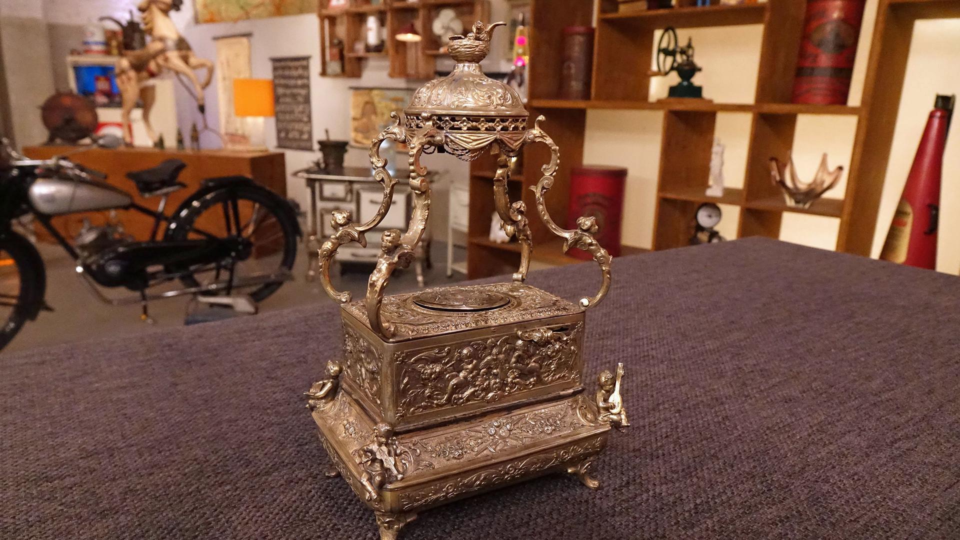 Auf einem mit Filz bezogenen Tisch steht ein metallener Singvogelautomat.