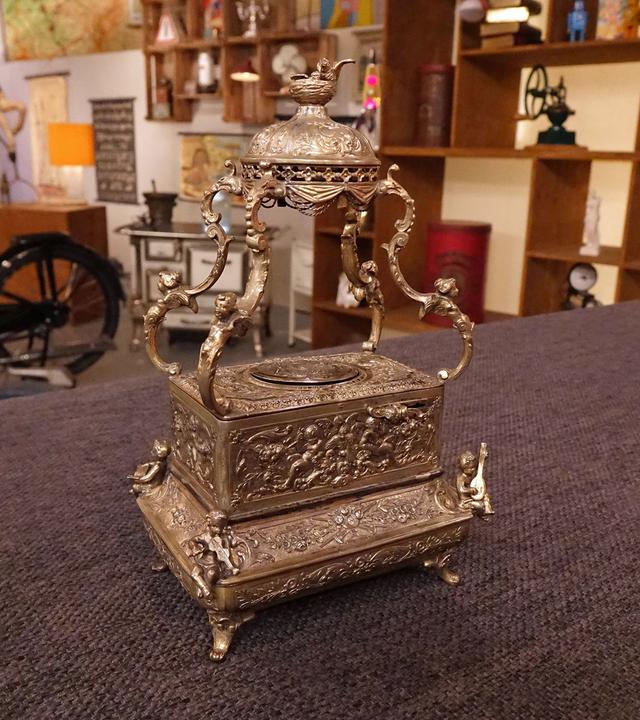 Auf einem mit Filz bezogenen Tisch steht ein metallener Singvogelautomat.