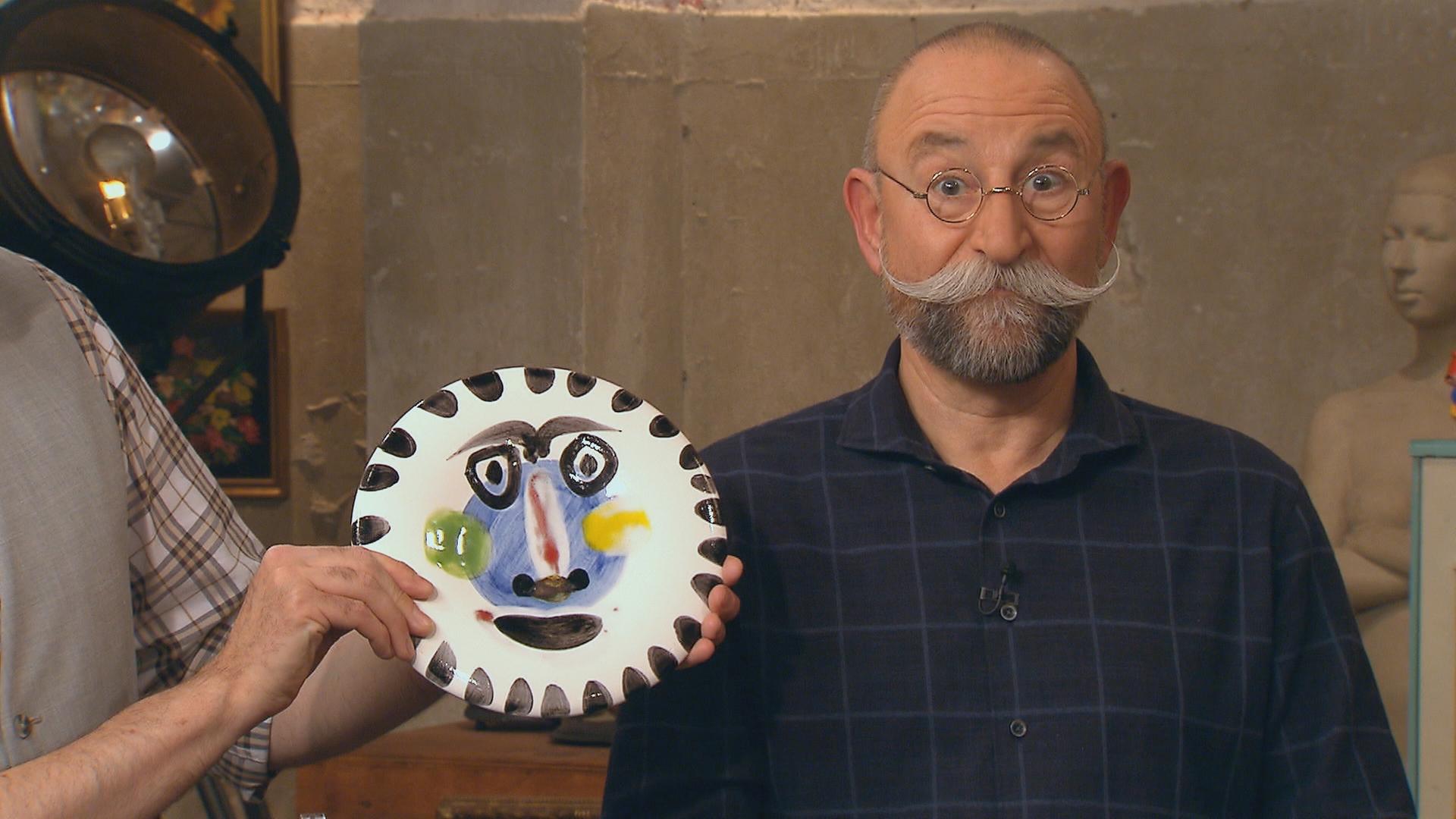 Experte Colmar Schulte-Goltz hält einen Teller von Pablo Picasso, der mit einem Gesicht bemalt ist, neben das Gesicht von Horst Lichter