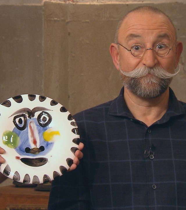 Experte Colmar Schulte-Goltz hält einen Teller von Pablo Picasso, der mit einem Gesicht bemalt ist, neben das Gesicht von Horst Lichter