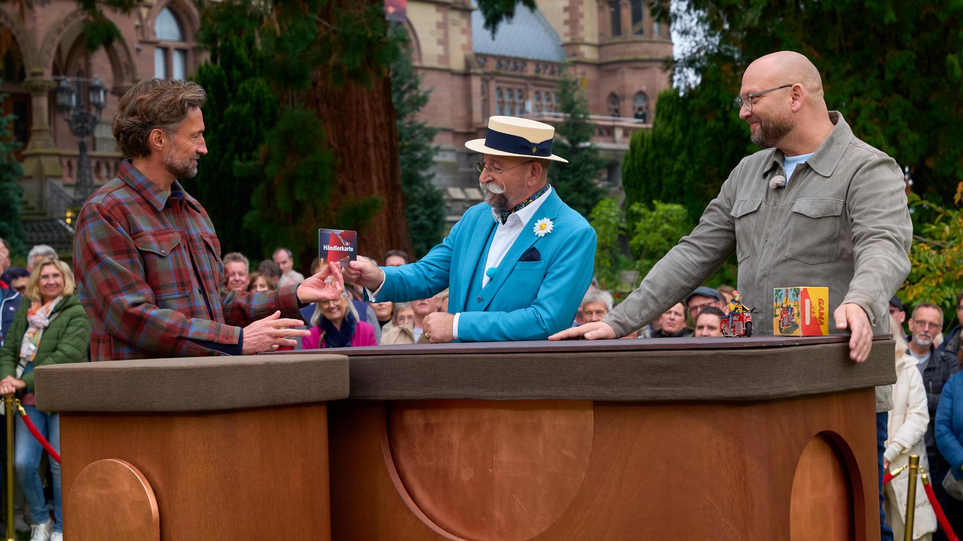 Horst Lichter überreicht Benjamin Sadler die Händlerkarte, daneben steht Sven Deutschmanek.