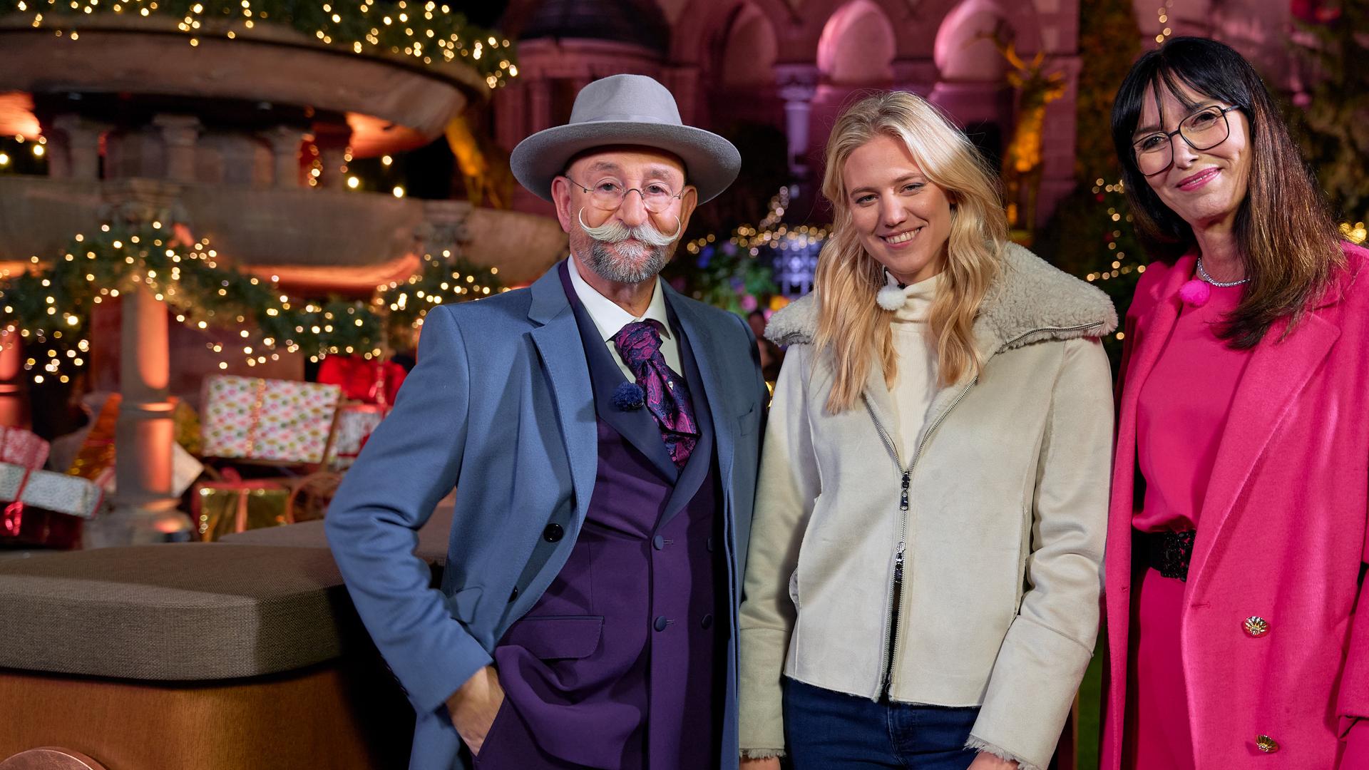 Horst Lichter, Larissa Marolt und Dr. Heide Rezepa-Zabel stehen vor dem Expertisenpult. Sie lächeln in die Kamera. Hinter ihnen ist weihnachtliche Dekoration zu sehen.