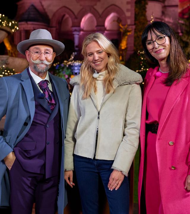 Horst Lichter, Larissa Marolt und Dr. Heide Rezepa-Zabel stehen vor dem Expertisenpult. Sie lächeln in die Kamera. Hinter ihnen ist weihnachtliche Dekoration zu sehen.