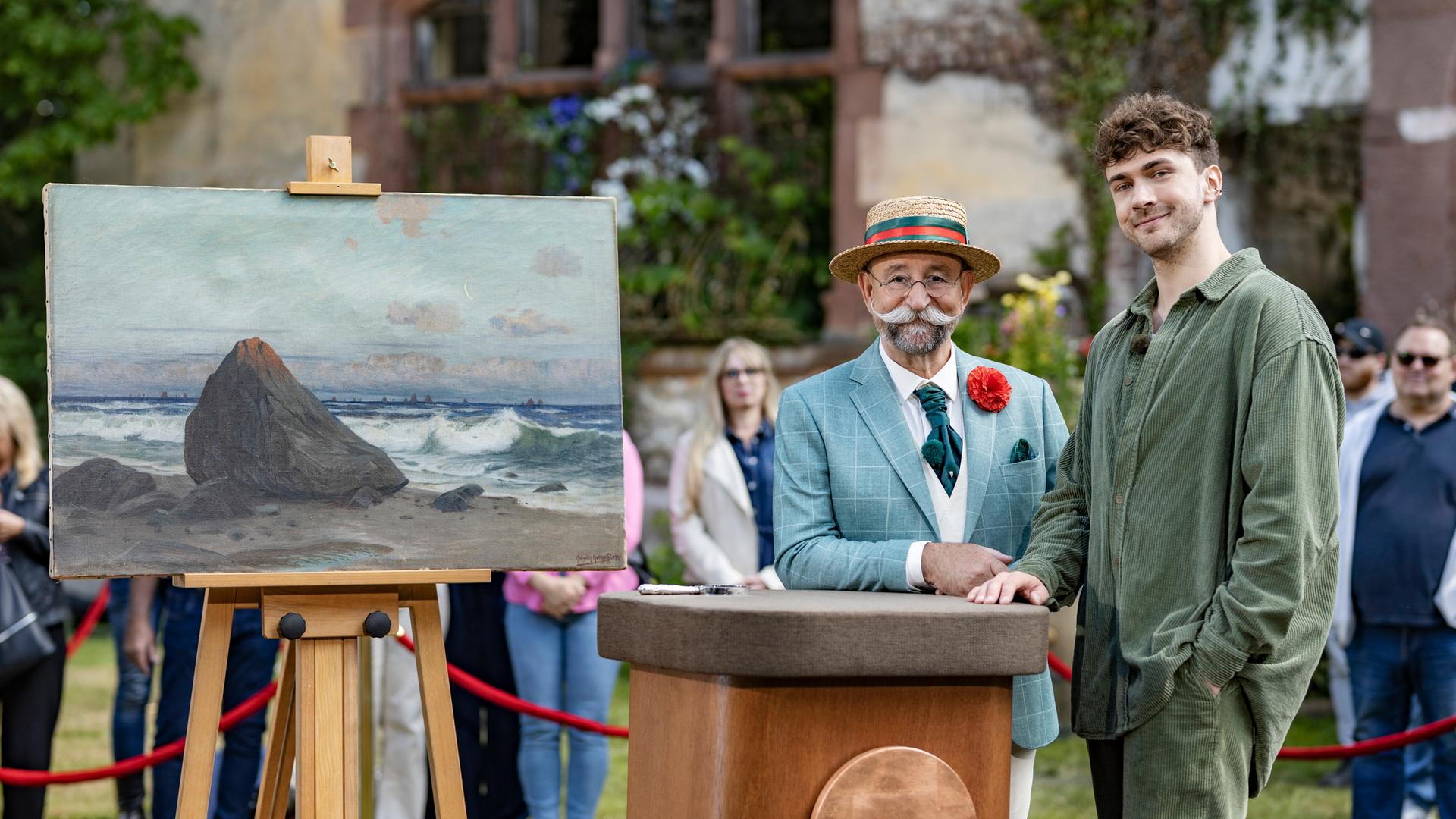 Timon Krause und Horst Lichter stehen nebeneinander am Expertisenpult und lächeln in die Kamera.