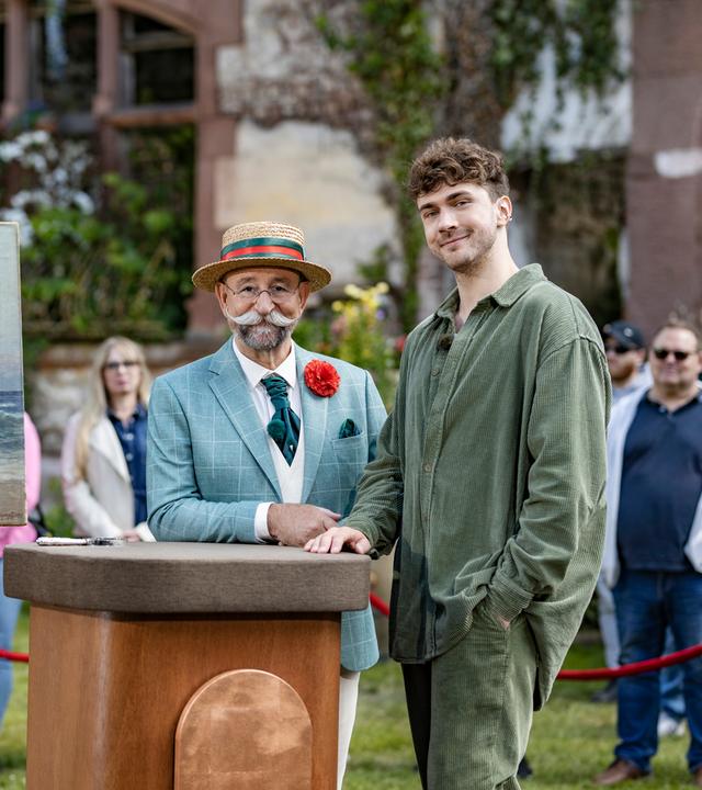 Timon Krause und Horst Lichter stehen nebeneinander am Expertisenpult und lächeln in die Kamera.
