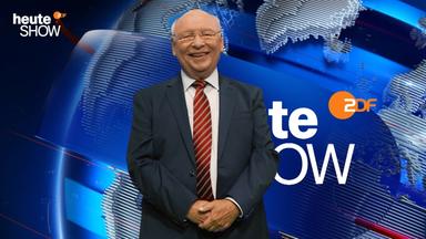 Vor dem blau leuchtenden Hintergrund der „heute-show“ lächelt Gernot Hassknecht in die Kamera. Der glatzköpfige Mann mit Brille trägt einen dunklen Anzug und eine rote Streifenkrawatte. Oben links sind der Schriftzug der Sendung und rechts das ZDF-Logo zu sehen.