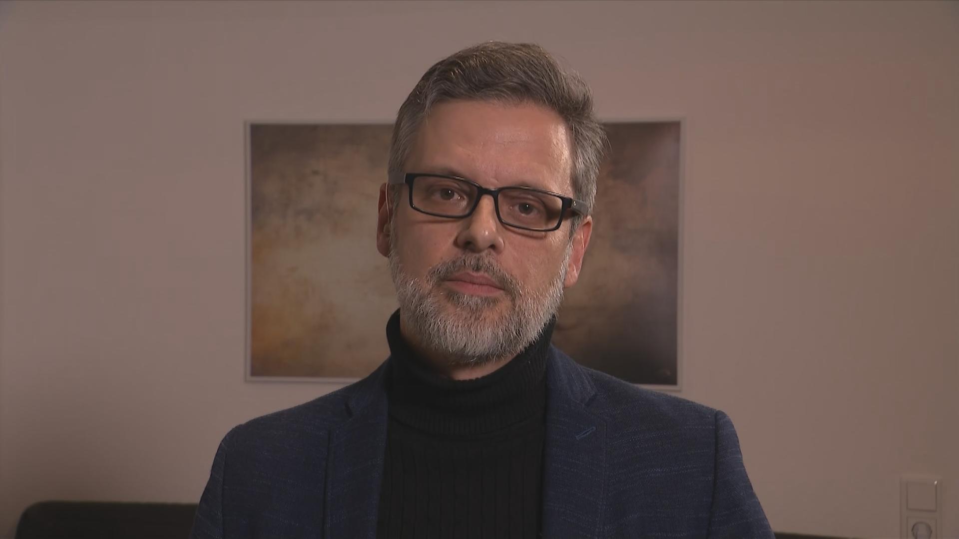 Der Psychologe Sebastian Bartoschek in seinem Privathaus, ein Mann mittleren Alters mit Brille, volles Haar und Bart, beides mit grauen Stränen durchzogen