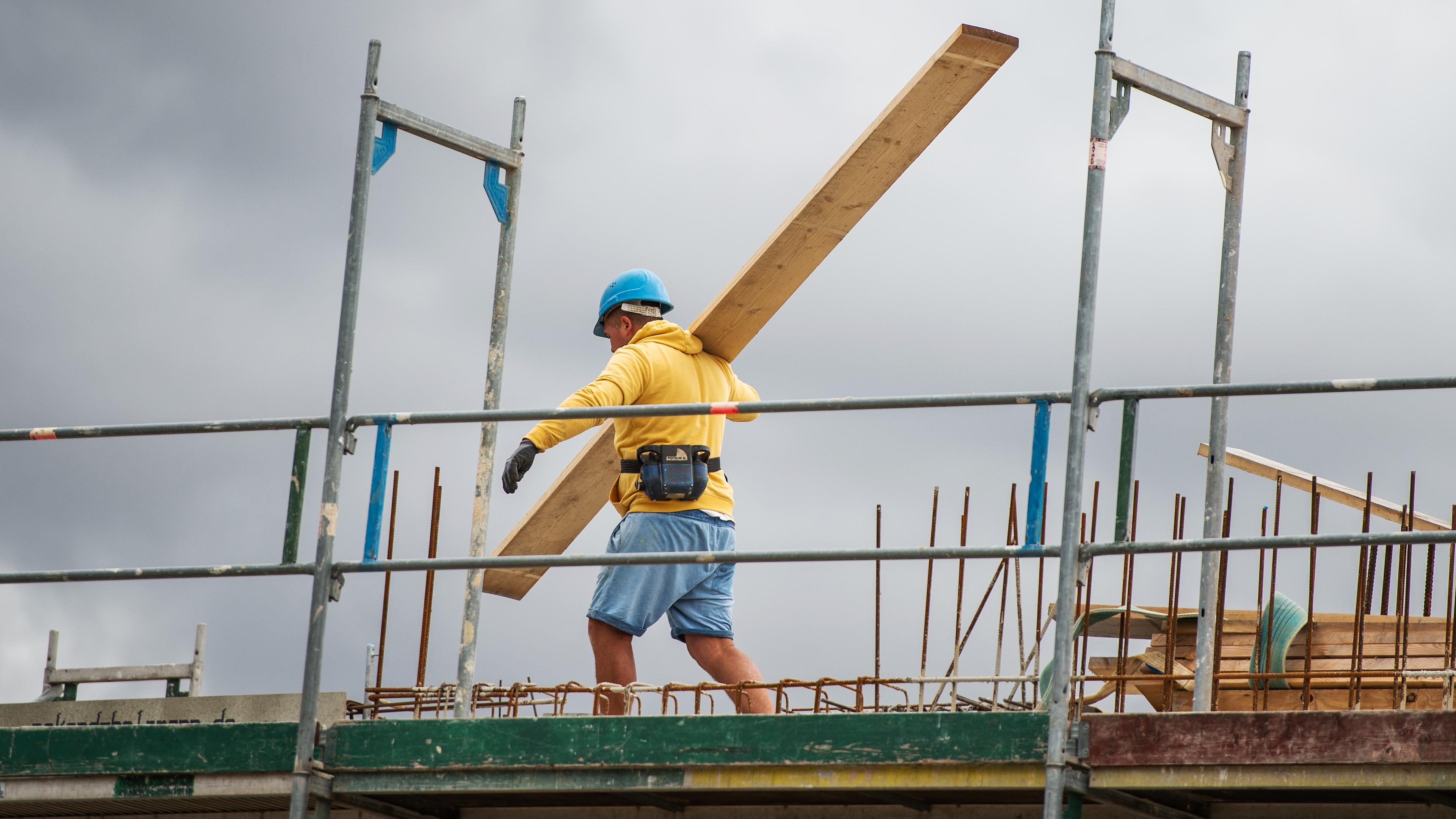 Ein bauarbeiter trägt auf einer Baustelle auf einem Hausdach ein Brett, aufgenommen am 08.07.2019