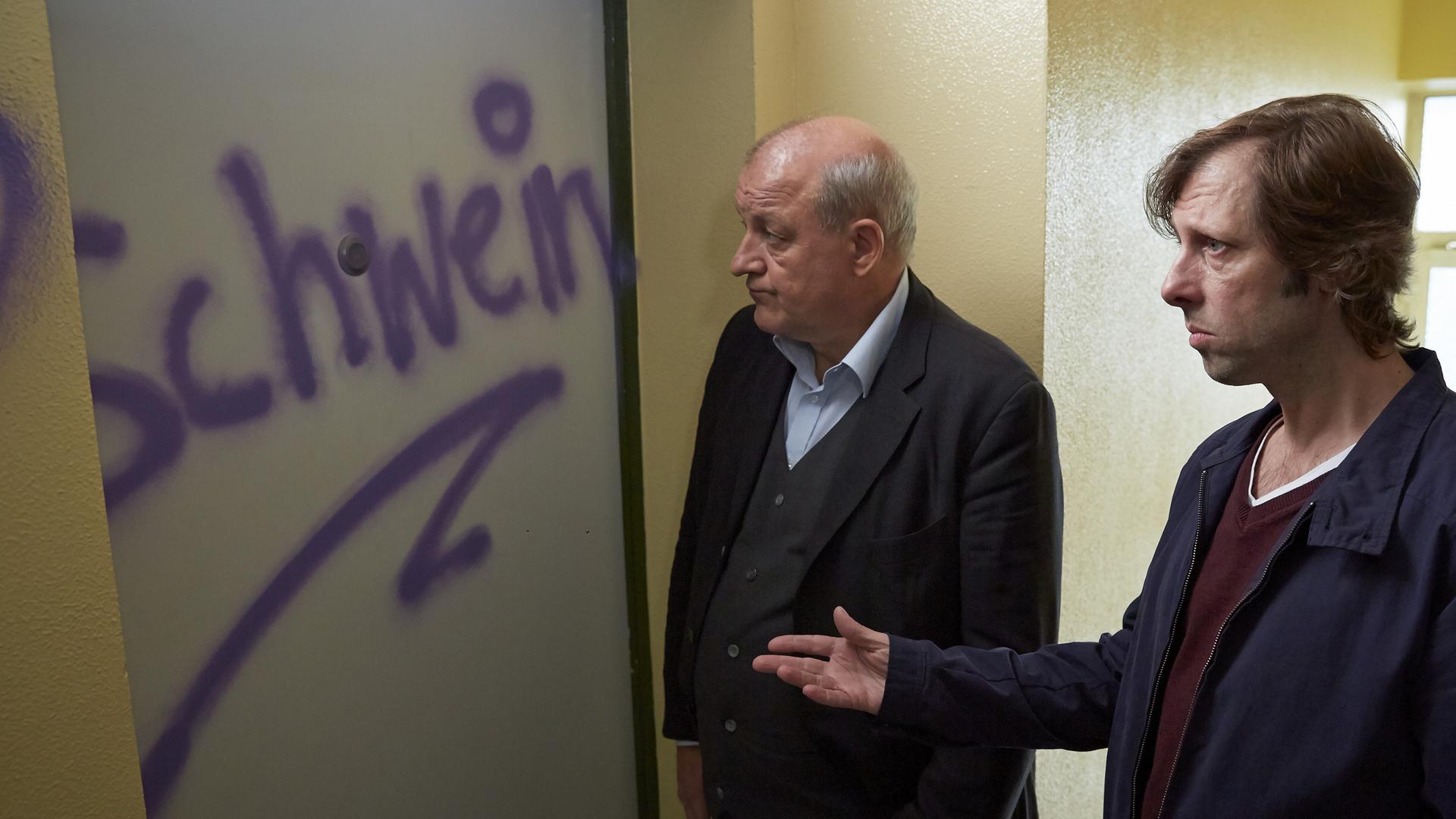 Georg Wilsberg (Leonard Lansink, l.) und Ekki Talkötter (Oliver Korittke, r.) stehen vor Ekkis Haustür, die mit einem Graffiti besprüht worden ist.