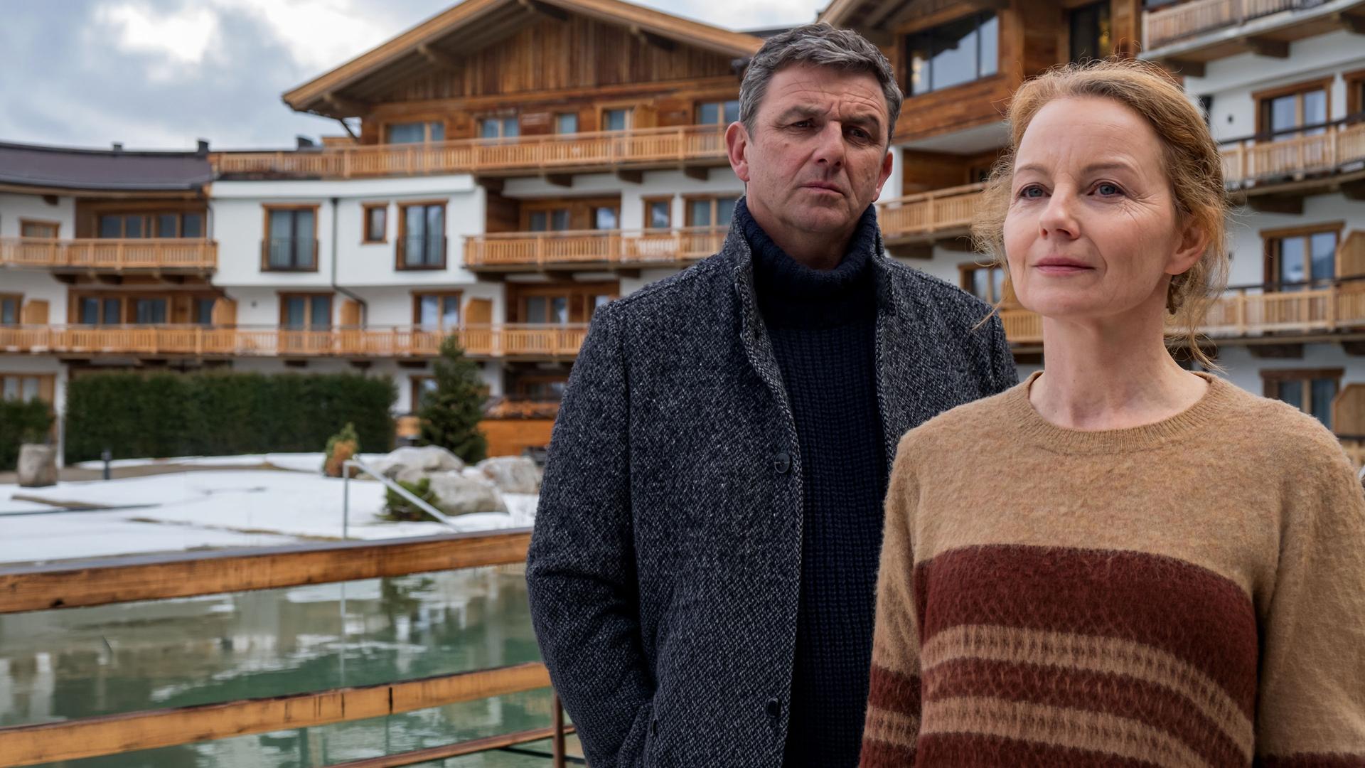 Vor einem Hotel steht Ella Kirchner (Carina Wiese) und blickt nachdenklich in die Ferne. Dr. Gruber (Hans Sigl) steht hinter ihr und blickt sie erwartungsvoll an.