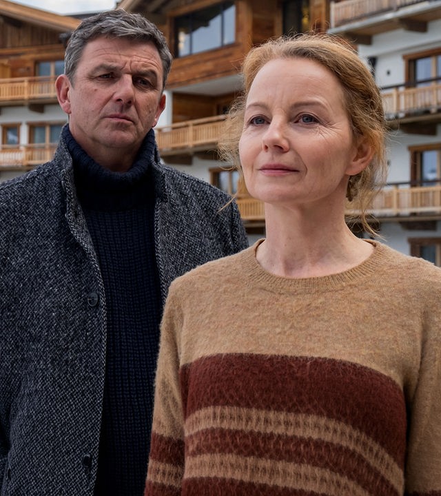 Vor einem Hotel steht Ella Kirchner (Carina Wiese) und blickt nachdenklich in die Ferne. Dr. Gruber (Hans Sigl) steht hinter ihr und blickt sie erwartungsvoll an.