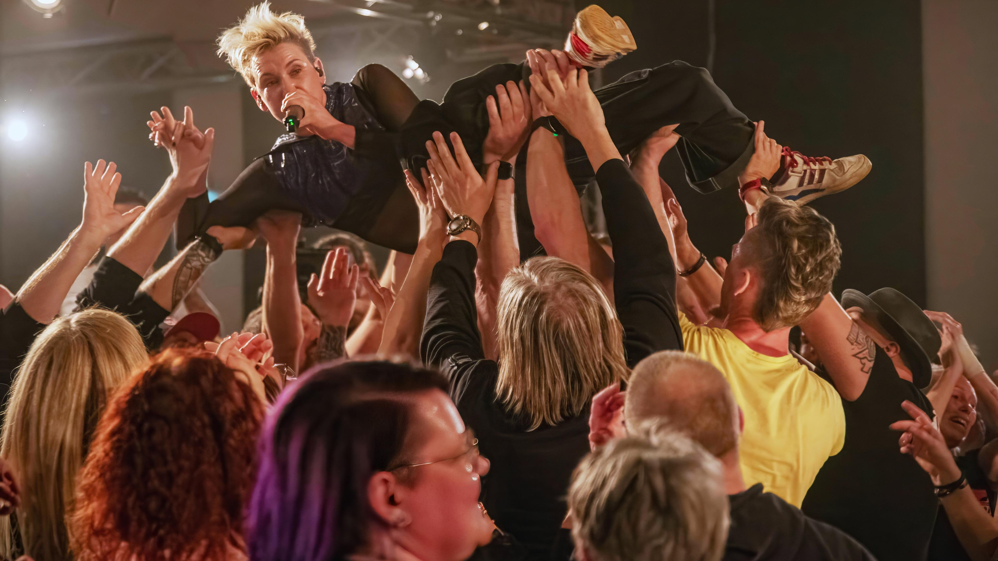 Eine Frau mit Mikrofon lässt sich von den Leuten vor der Bühne tragen.