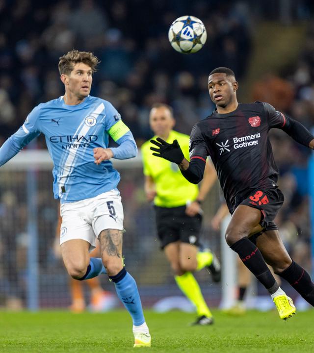 John Stones (Manchester City) und Christian Kofane (Bayer Leverkusen) kämpfen. 