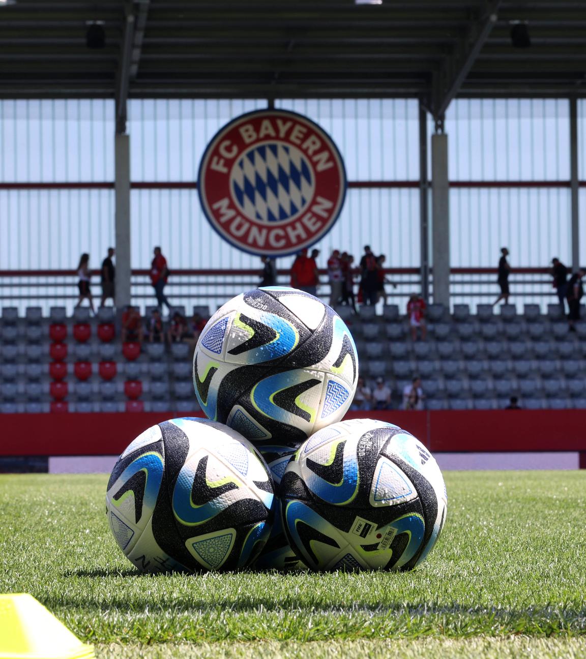 Drei Bälle aufeinander aufgestapelt, im Hintergrund das Logo des FC Bayern