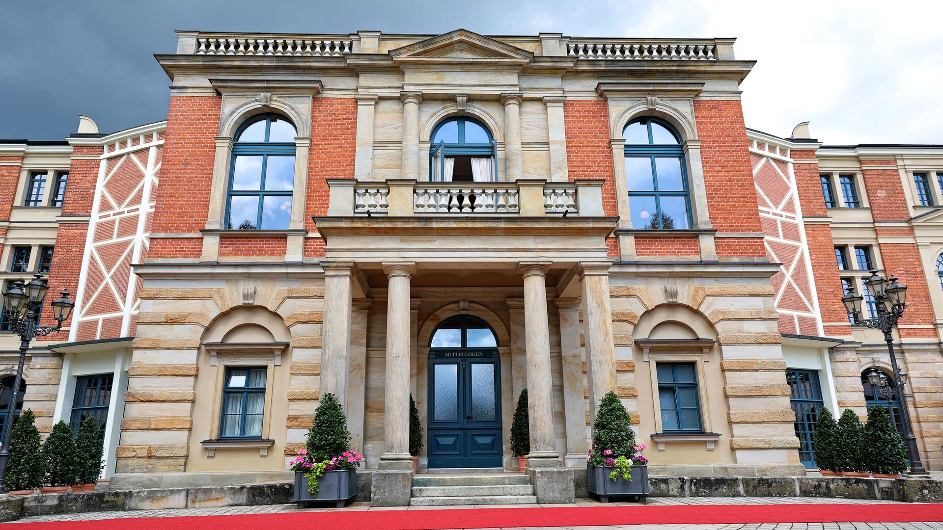 Ein großes zweistöckiges historisches Gebäude aus roten Backsteinen und sandfarbenem Stein mit Säuleneingang und Balkon im oberen Stockwerk.
