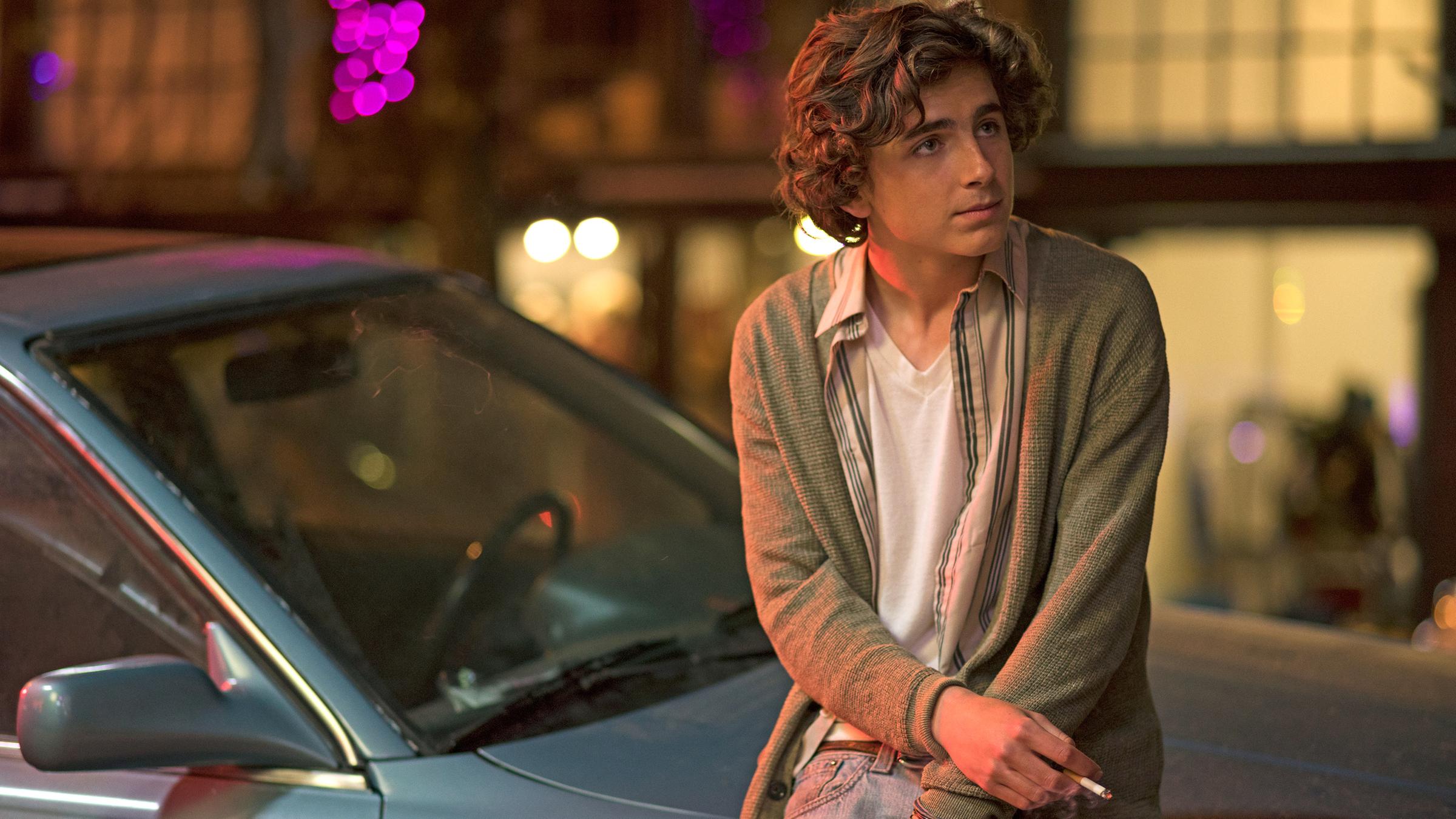 In leicht zusammengesunkener Körperhaltung, als würde er frieren, steht Nic (Timothée Chalamet) angelehnt an die Motorhaube eines Autos nachts auf einer Straße. In der rechten herabhängenden Hand hält er eine Zigarette.