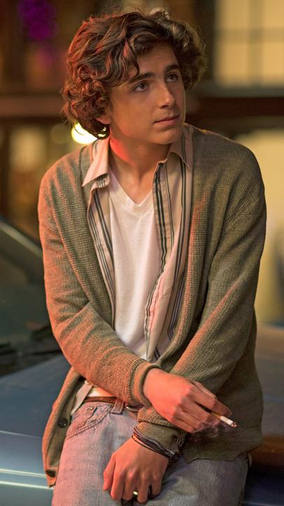 In leicht zusammengesunkener Körperhaltung, als würde er frieren, steht Nic (Timothée Chalamet) angelehnt an die Motorhaube eines Autos nachts auf einer Straße. In der rechten herabhängenden Hand hält er eine Zigarette.