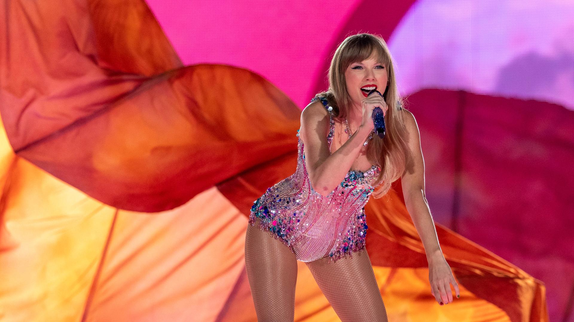 Taylor Swift steht in einem schwarzen, goldverzierten Bühnenkostüm vor zwei großen, aufgerichteten Schlangenfiguren auf einer Bühne.