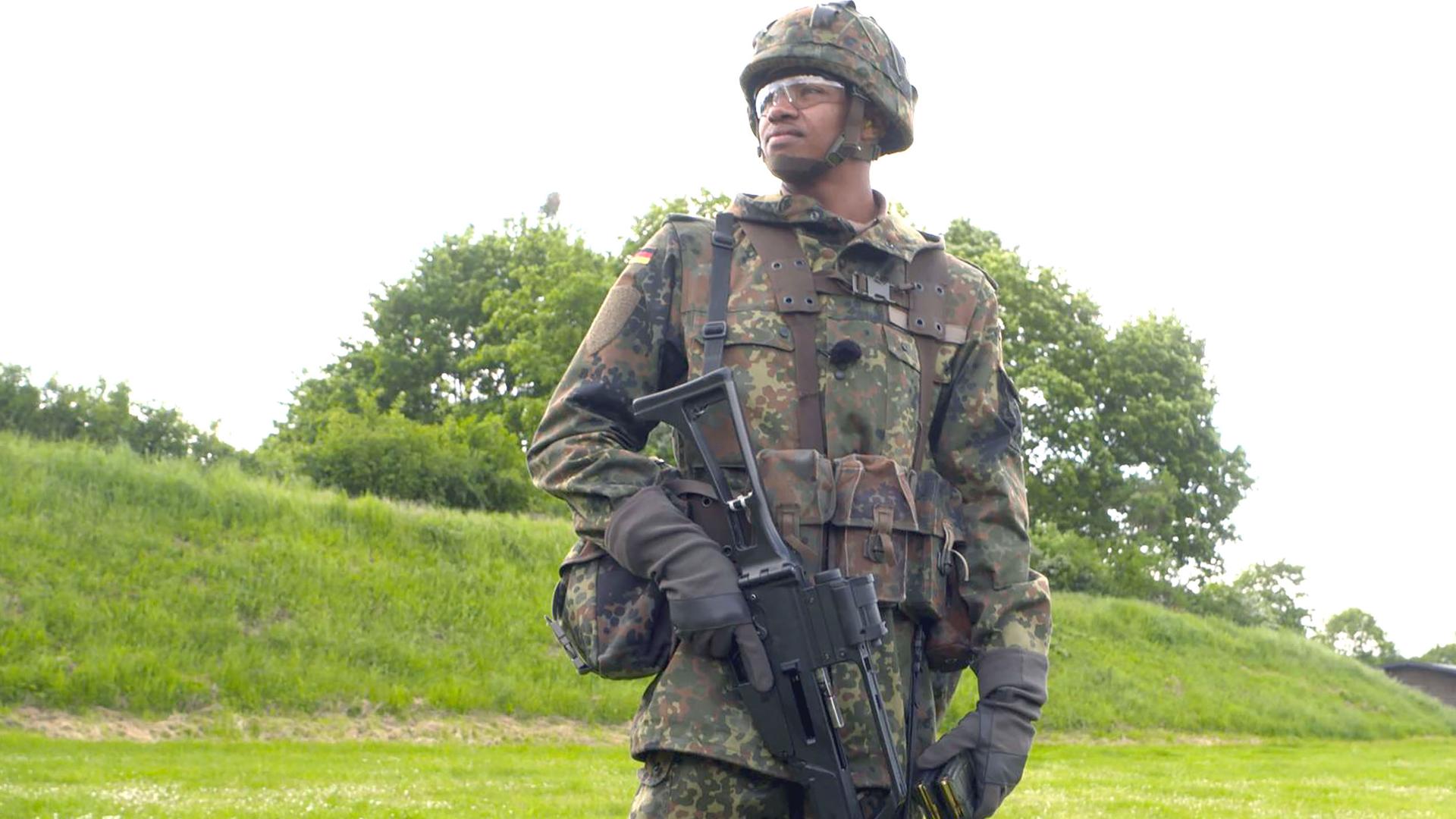 Leon hat seine Felduniform an und steht auf einer grünen Wiese.