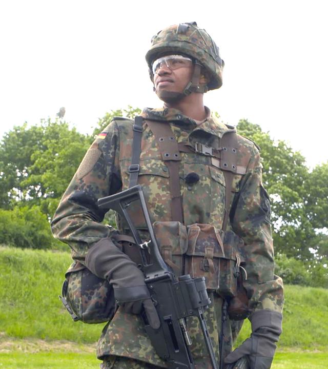 Leon hat seine Felduniform an und steht auf einer grünen Wiese.