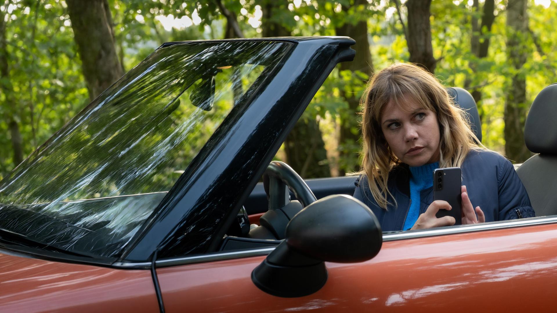 „Neuer Wind im Alten Land – Beke wirbelt auf“: Beke (Felicitas Woll) sitzt in ihrem offenen Cabrio und macht aus dem Auto heraus ein Bild mit ihrem Handy.