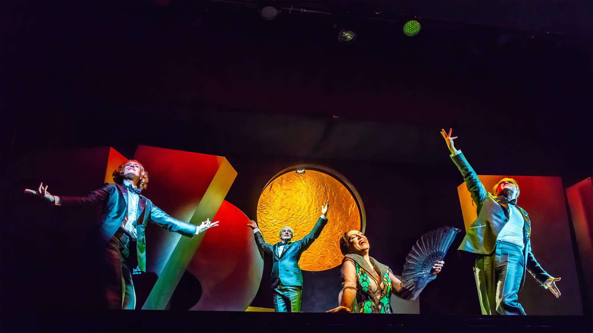 Auf einer dunklen Bühne mit hell angeleuchteten großen Objekten bewegen sich tanzend mehrere Personen.