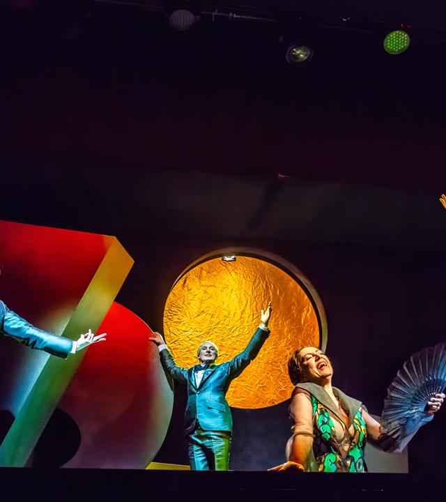 Auf einer dunklen Bühne mit hell angeleuchteten großen Objekten bewegen sich tanzend mehrere Personen.