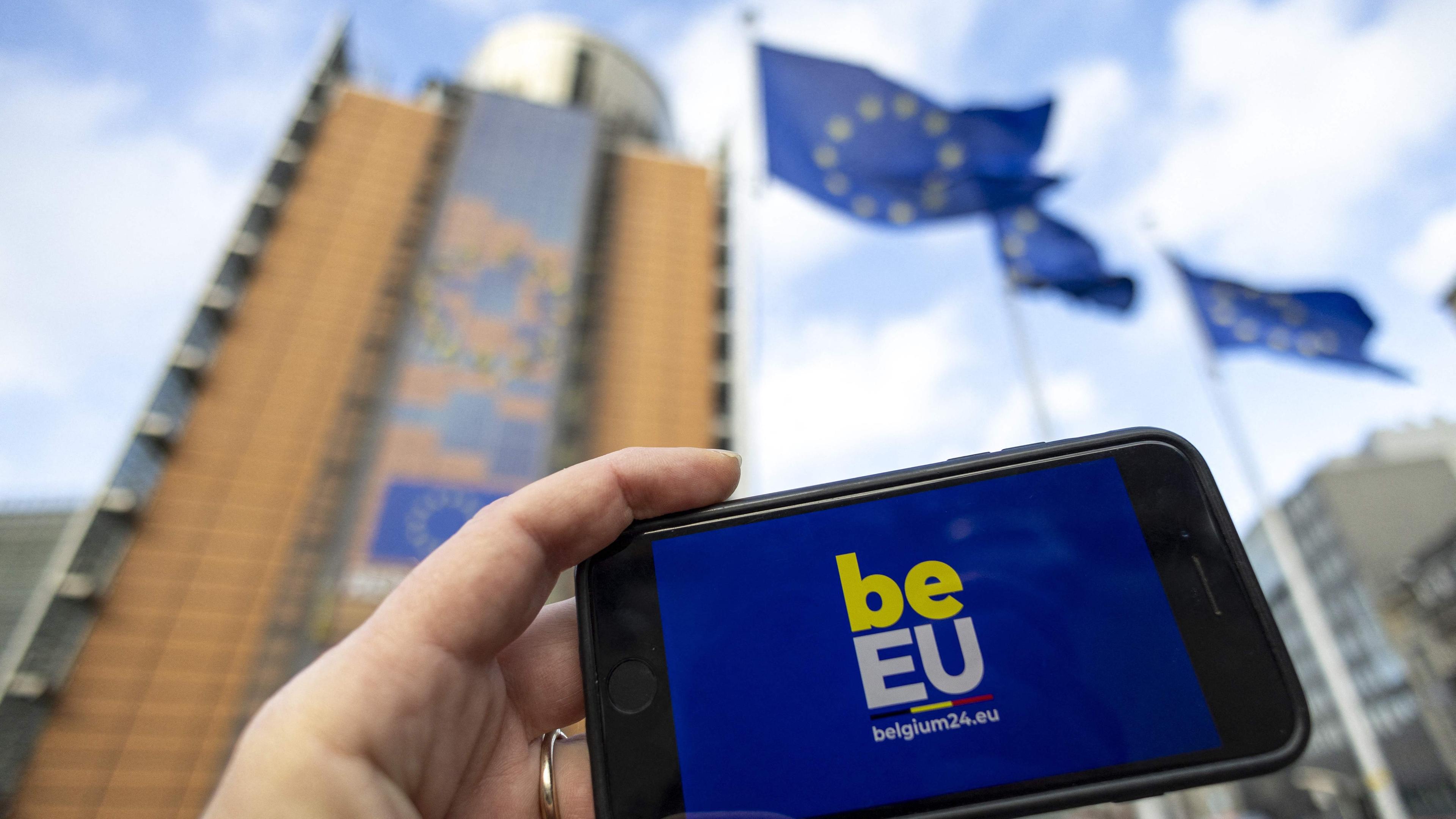 Ein Smartphone mit dem Logo der belgischen EU-Ratspräsidentschaft vor dem Sitz der Europäischen Union in Brüssel.