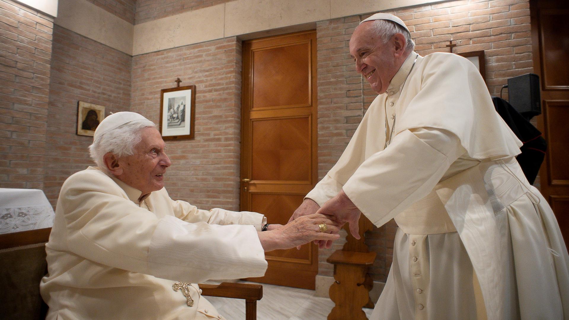 Papst Benedikt XVI. und Papst Franziskus reichen sich die Hände im Vatikan.