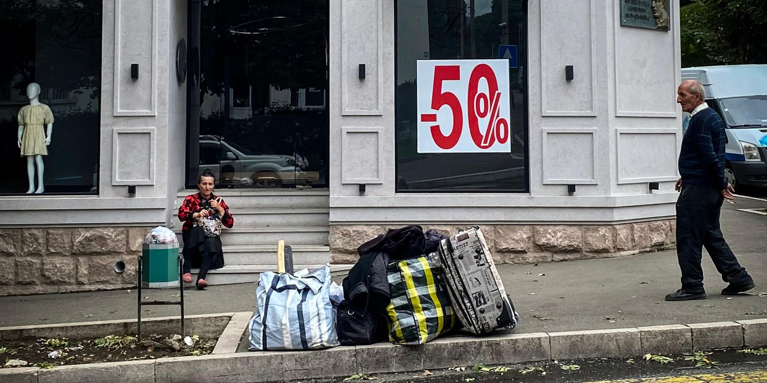 Eine Frau wartet mit gepackten Tüten vor einem Geschäft auf ihre Ausreise aus Aserbaidschan