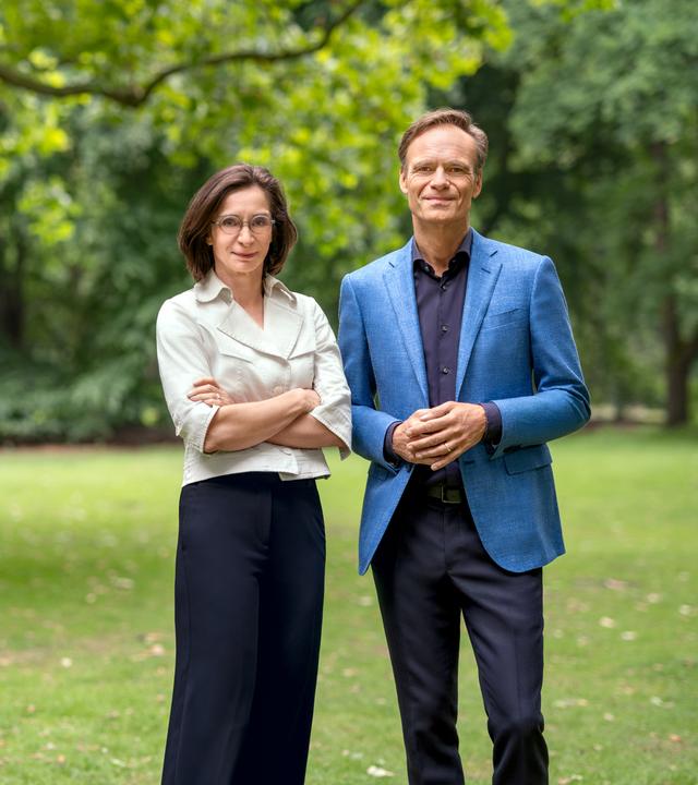 Diana Zimmermann und Wulf Schmiese stehen vor Bäumen auf einer grünen Wiese nebeneinander und blicken in die Kamera.