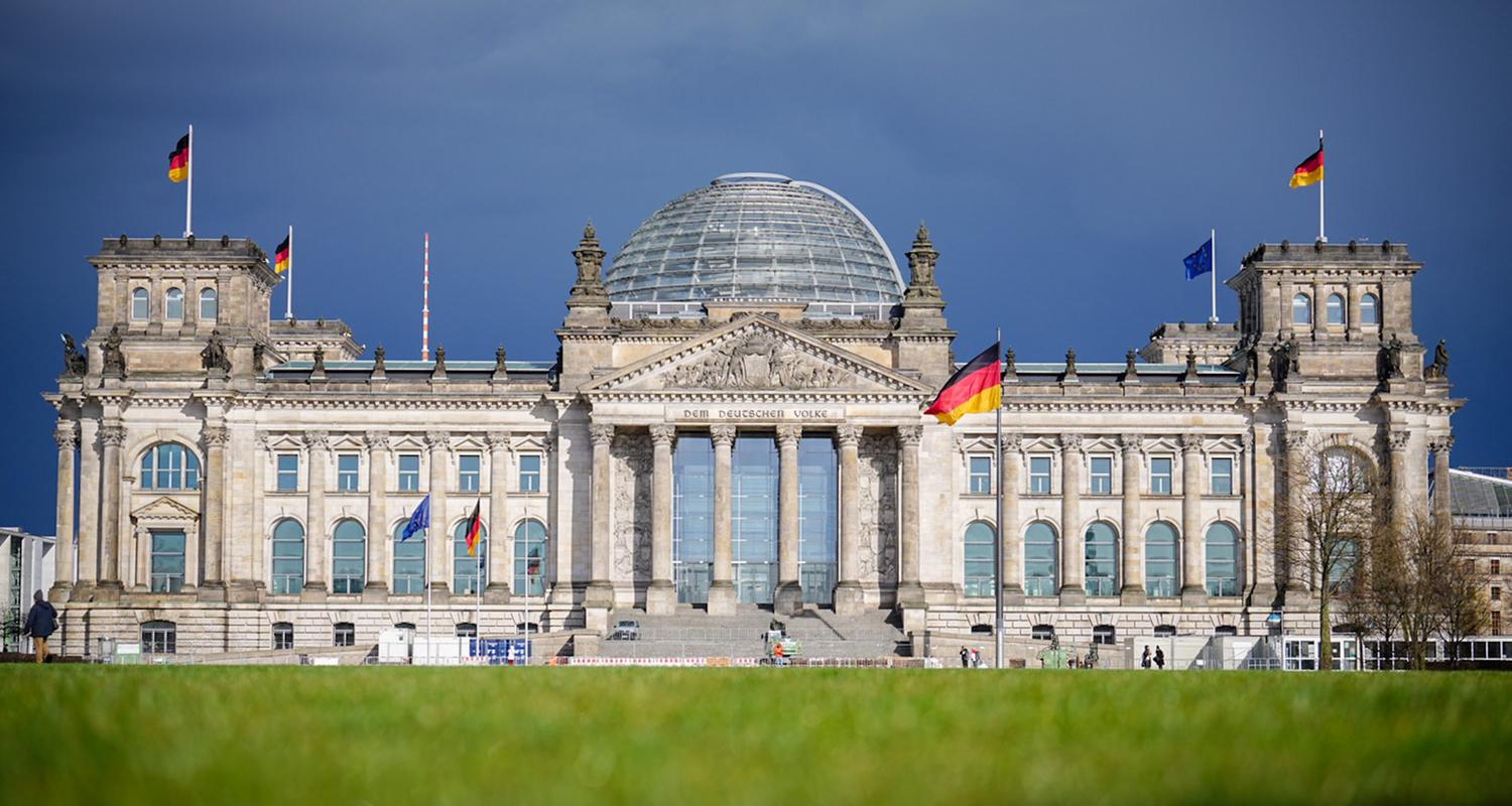 Das Reichstagsgebäude leuchtet im Sonnenschein unter dem dunklen Himmel.