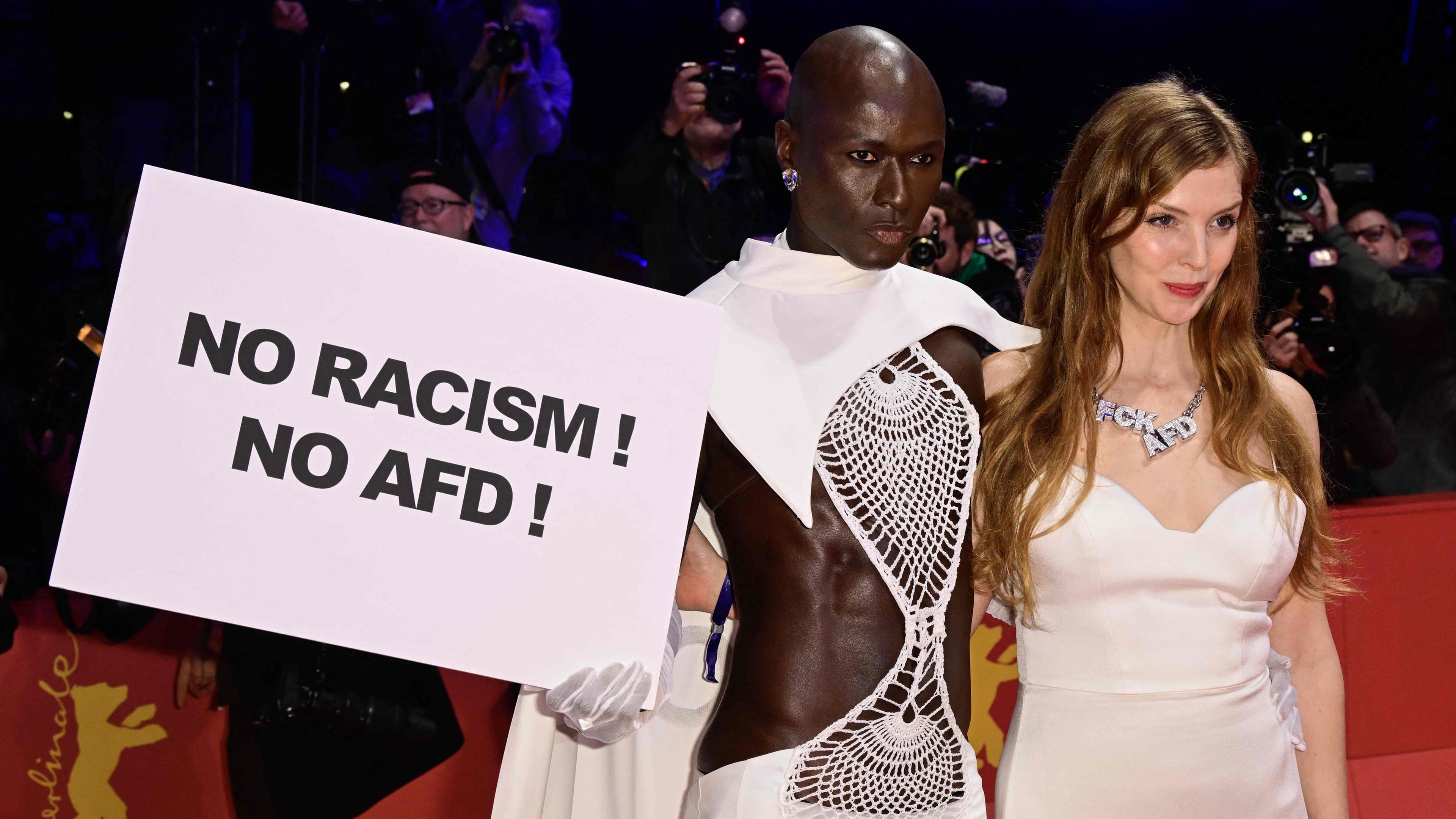 Papis Loveday posiert auf dem roten Teppich mit einem Plakat mit der Aufschrift "No racism no AfD" mit der deutschen Schauspielerin Pheline Roggan, die eine Halskette mit der Aufschrift "FCK AFD" trägt, vor der Eröffnungszeremonie der 74. Berlinale, Europas erstem großen Filmfestival des Jahres, in Berlin am 15.02.2024.