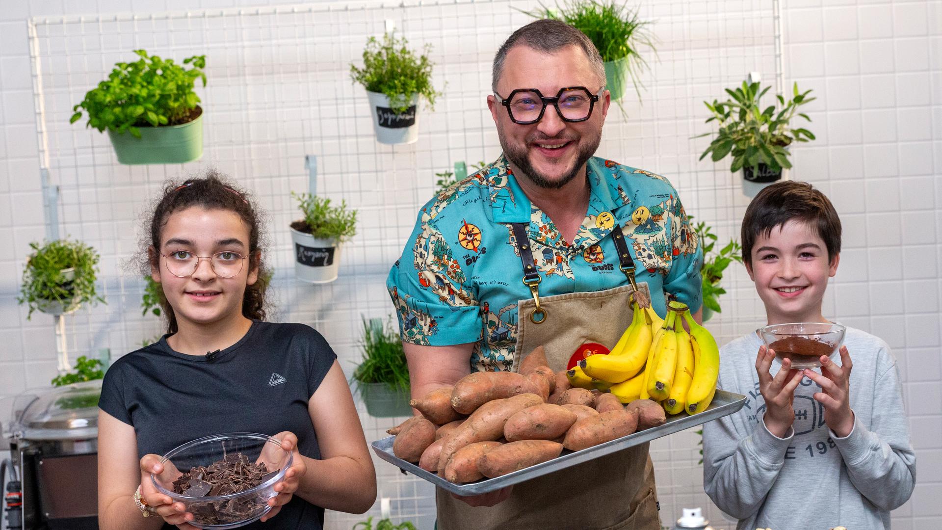 Sebastian Lege und zwei Kinder halten Bananen, Süßkartoffeln und Schokolade in die Kamera.