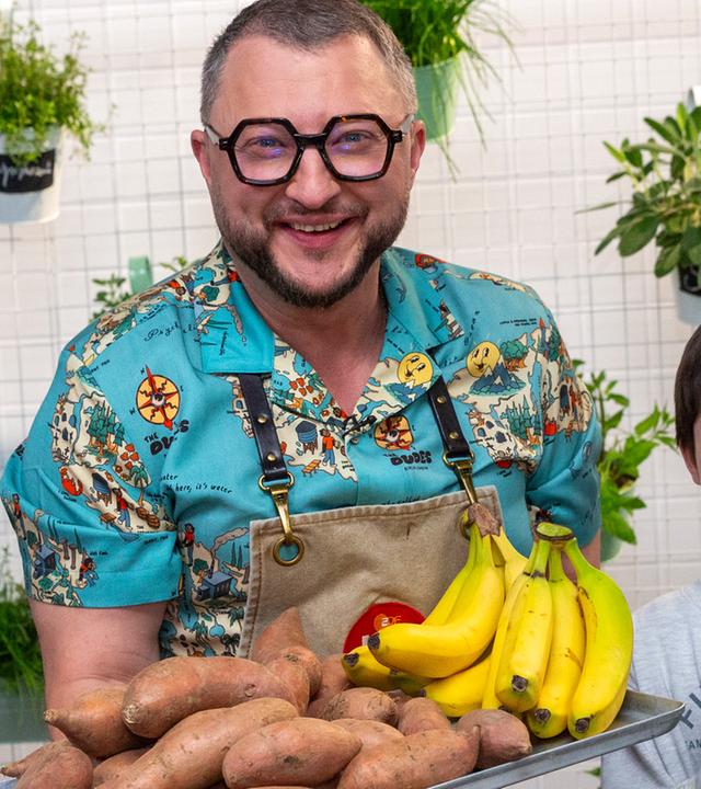 Sebastian Lege und zwei Kinder halten Bananen, Süßkartoffeln und Schokolade in die Kamera.