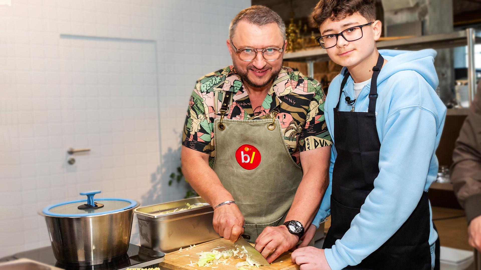 besseresser Kids - Lege packt´s an: Sebastian Lege steht gemeinsam mit einem Schüler in der Schulküche und schnippelt Gemüse. 