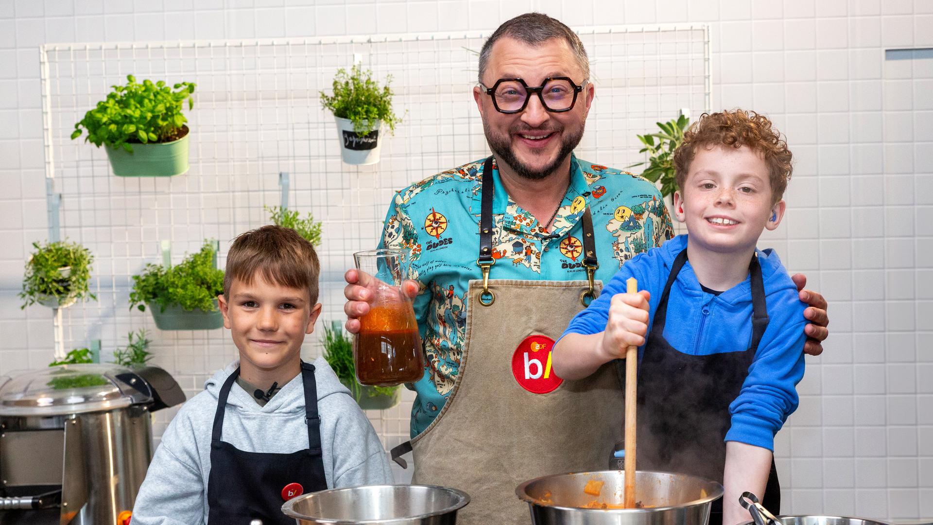 besseresser kids: Lege packt´s an: Sebastian Lege steht mit zwei Schülern am Herd und vor den Kochtöpfen. 