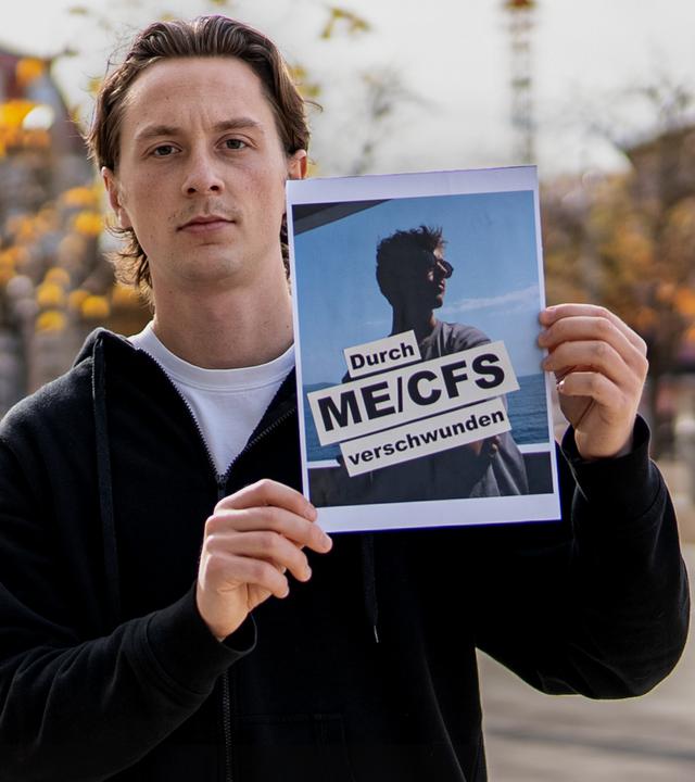 Jonas hält ein Bild von seinem besten Freund, Tom mit dem Schriftzug "Durch ME/CFS verschwunden" in der Hand und zeigt es in die Kamera