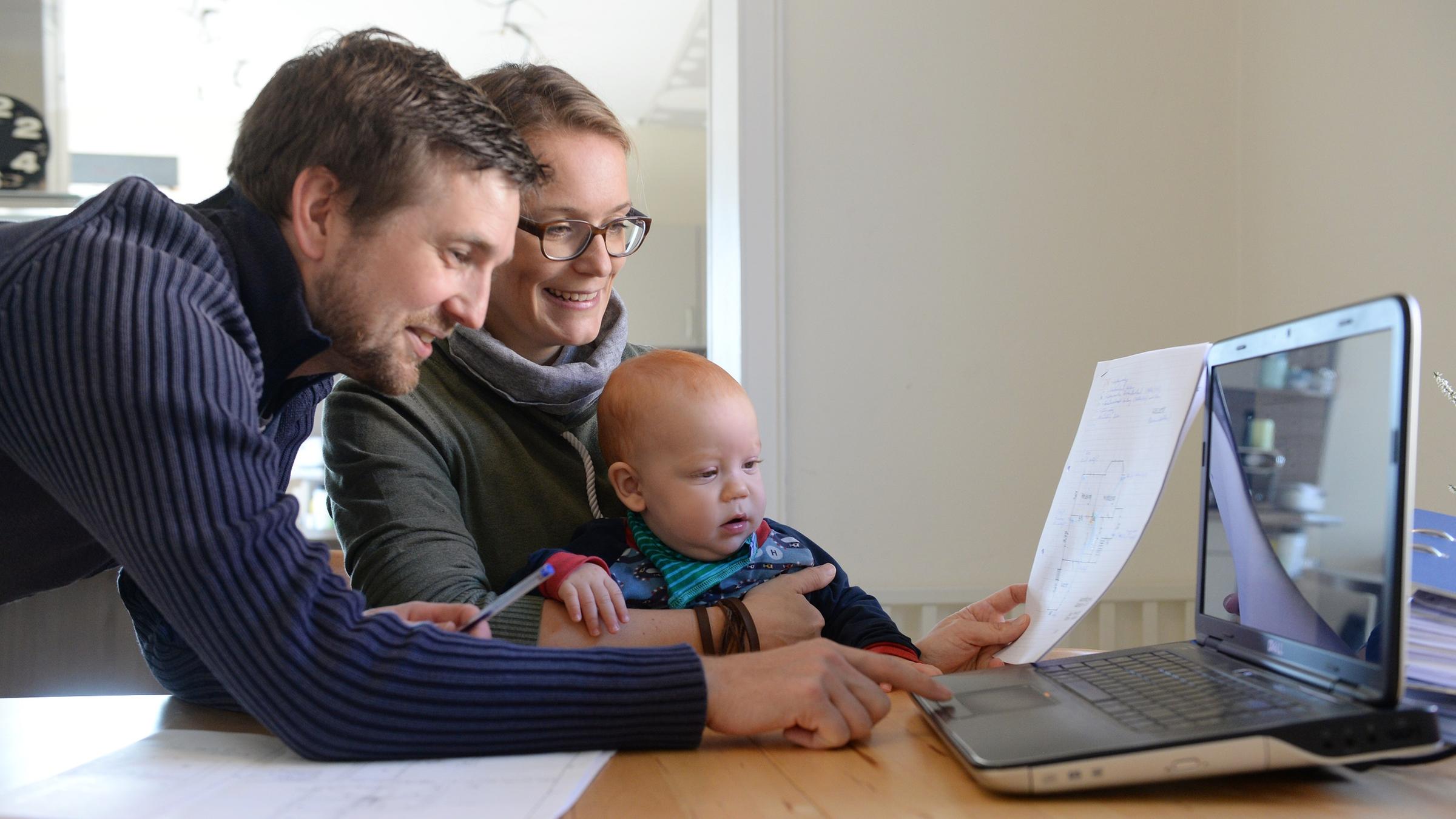 Eltern mit ihrem Säugling prüfen ihre Betriebskostenabrechnung mit dem Laptop.