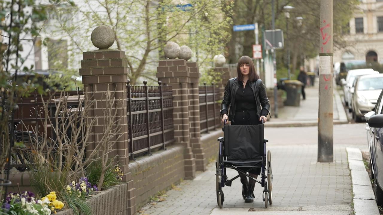 Betroffene von Folgen nach-Corona-Impfung, die ihren Rollstuhl auf einem Gehweg schiebt