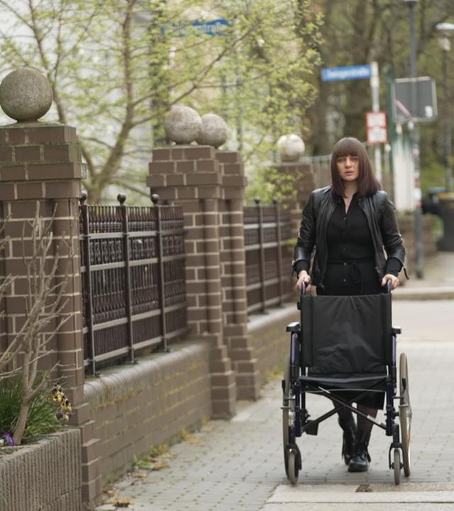 Betroffene von Folgen nach-Corona-Impfung, die ihren Rollstuhl auf einem Gehweg schiebt