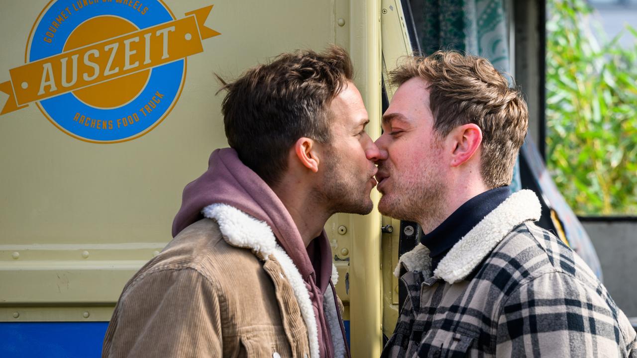 Dr. Paul Eckart (Florian Frowein) und Ron Berger (Moritz von Zeddelmann) stehen sich am Kioskwagen gegenüber und geben sich einen Kuss. Den gelben Kioskwagen ziert ein Logo mit der blau-gelben Aufschrift "Auszeit Gourmet Lunch On Wheels Aachens Food Truck".