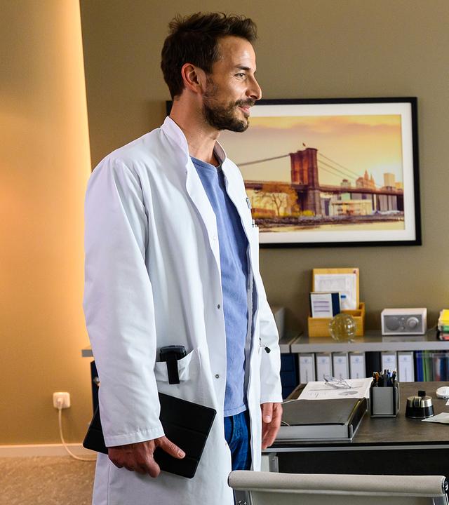 Dr. Frank Stern (Max Alberti) steht in Prof. Dr. Alexander von Arnstetts (Florian Fitz) Büro und spricht mit dem, auf einem Stuhl sitzenden, Dr. Tom Koopmann (Tobias Licht). Dr. von Arnstett beobachtet die Szene von seinem Schreibtischstuhl aus.