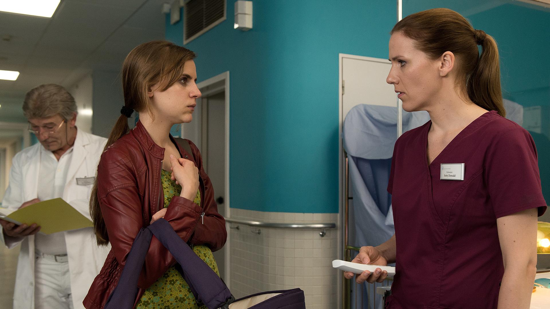 Karla (Marie Mayer) trägt ihr Baby in einer Babytasche in die Klinik zu Betty (Bettina Lamprecht)