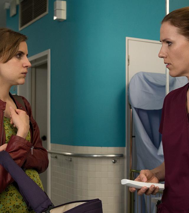 Karla (Marie Mayer) trägt ihr Baby in einer Babytasche in die Klinik zu Betty (Bettina Lamprecht)
