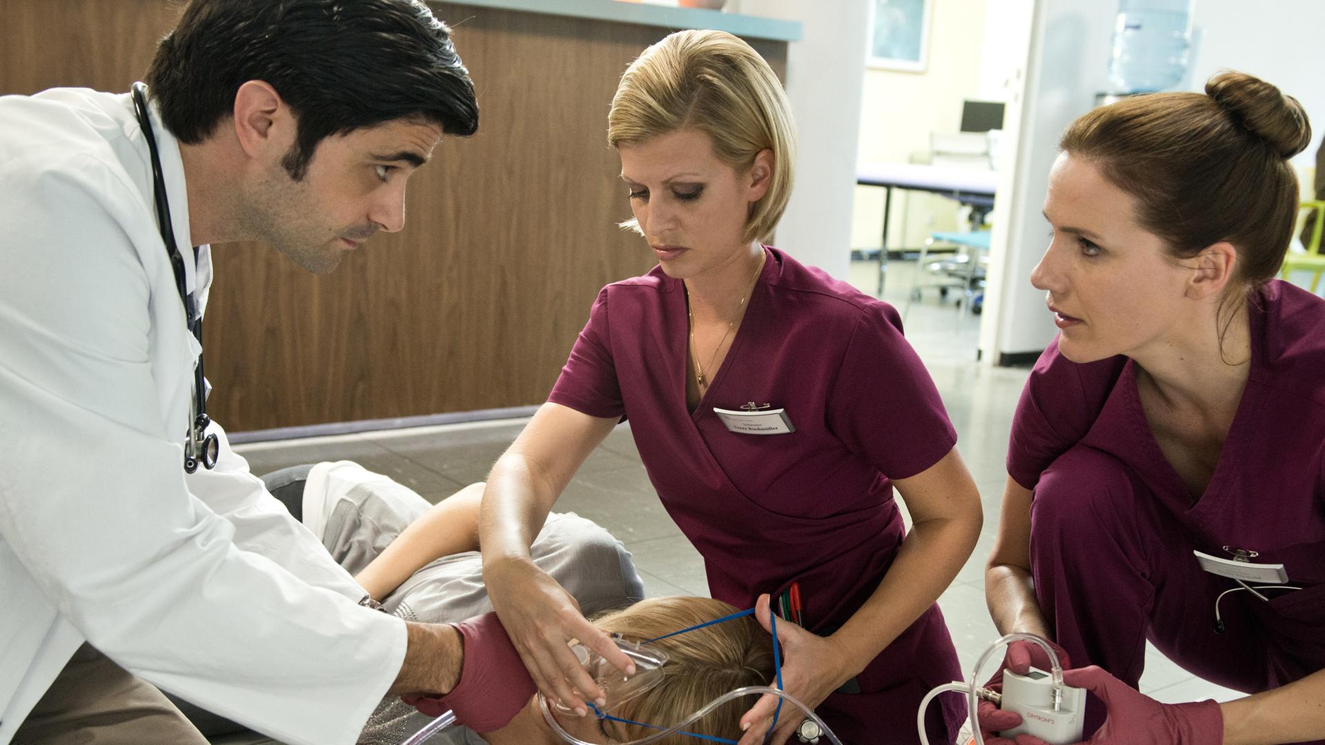 Dr. Behring (Maximilian Grill), Lizzy (Theresa Underberg) und Betty (Bettina Lamprecht) leisten erste Hilfe bei der Patientin Frau Tessmer (Gruschenka Stevens) auf dem Flur in der Karlsklinik.