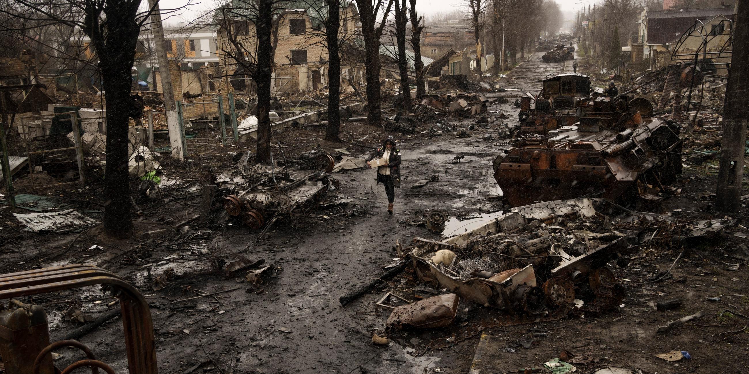 Eine Frau geht inmitten zerstörter russischer Panzer in Butscha am Stadtrand von Kiew, aufgenommen am 03.04.2022