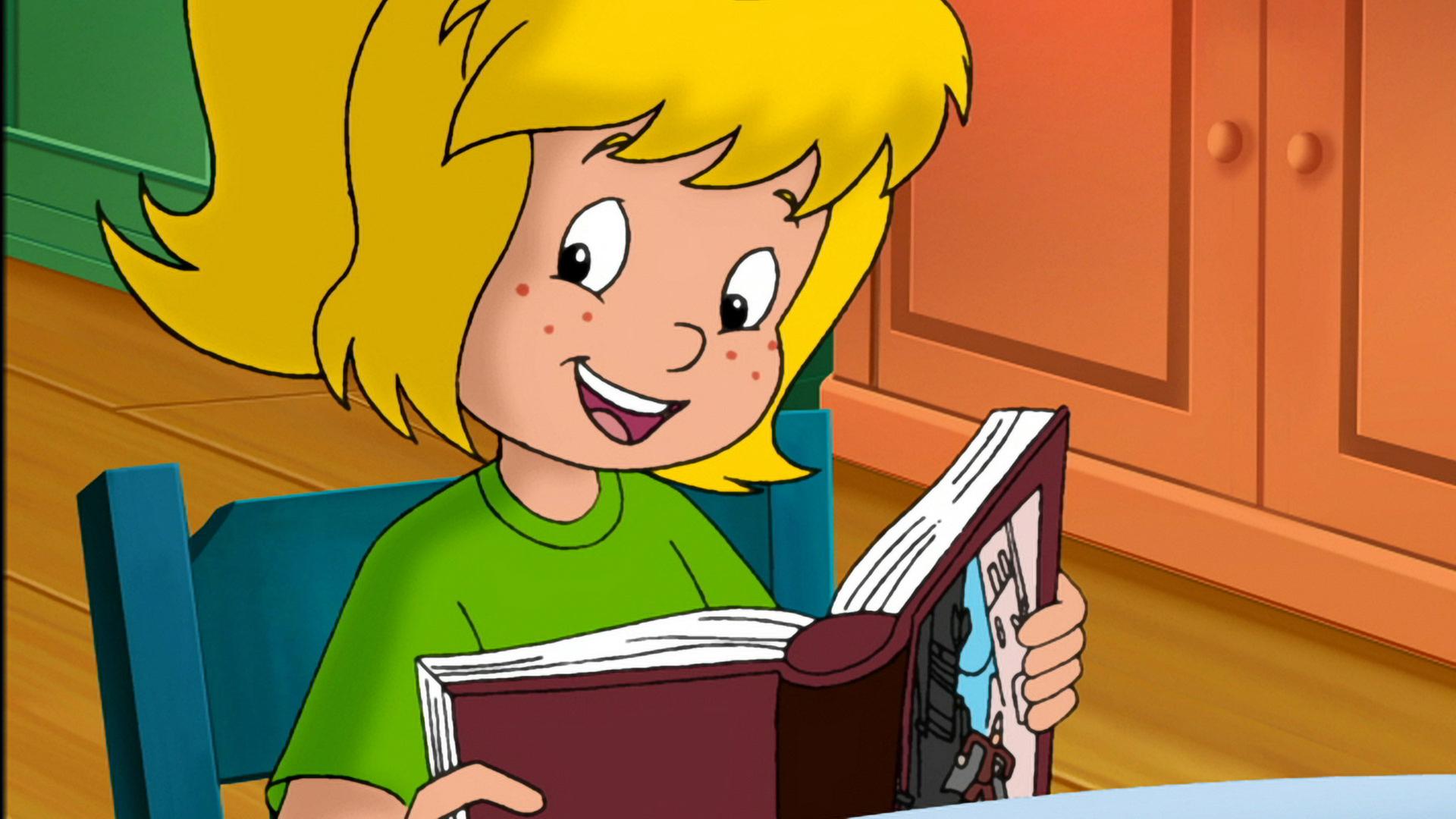 Bibi liest aus einem Buch vor. Sie schaut fröhlich in das vor ihr aufgeklappte Buch.