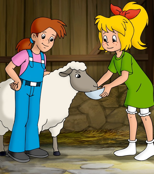 Bibi und Margie stehen in einem Schafstall vor einem Schaf. Bibi hält es eine Schale hin, aus dem es trinkt.