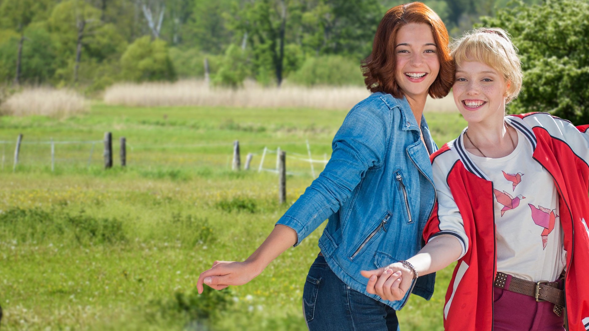 Bibi & Tina stehen auf einer Koppel und lächeln in die Kamera